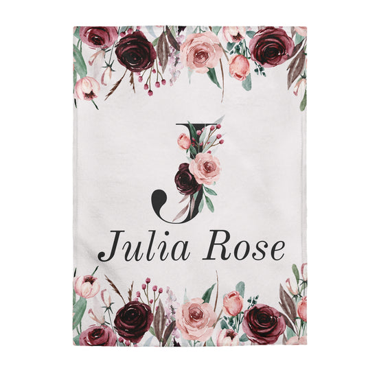 This personalized flower baby blanket has the baby's first initial in the middle. The initial is a J with burgundy and light pink roses with leaves on the J. The name on the blanket is Julia Rose underneath the initial. On the top and bottom have light pink and burgundy roses with leaves.